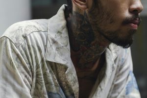 Close-up of a man with a striking neck tattoo in a casual floral shirt, showcasing individuality.